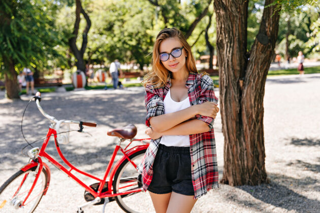 自然时髦的欧洲女人在街上和自行车合影温文尔雅的女模特拿着红色自行车站在公园里微笑休闲时尚