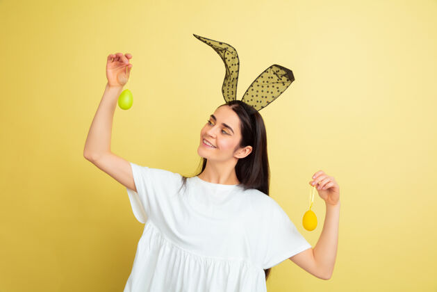 有趣白人妇女作为一个复活节兔子在黄色工作室背景复活节快乐的问候自信节日耳朵