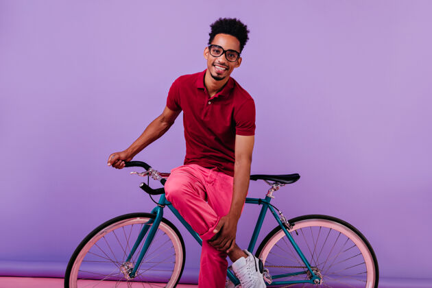 成人微笑害羞的非洲男人穿着粉色裤子和自行车合影英俊的黑人男人孤立快乐着装卷发