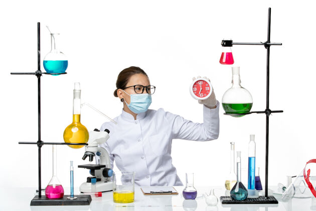 实验室前视图：身穿医疗服的女化学家 戴着面具 白色背景上拿着时钟病毒实验室化学科维德飞溅医生医学化学