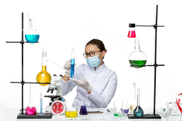 正面前视图穿着医疗服的女化学家 戴着面罩 白色背景上拿着蓝色溶液 飞溅着病毒化学实验室的病毒医学喷溅视图