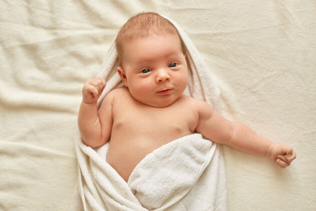 人的脸宝宝洗完澡躺在床上的白色毯子上 看着相机 裹着毛巾 宝宝洗完澡 可爱的新生宝宝清洁大笑微笑