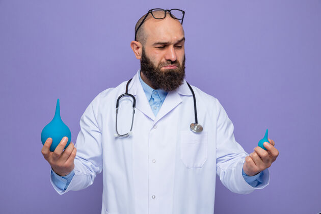 脖子一个留着胡子的医生 穿着白大褂 脖子上戴着听诊器 手里拿着医用梨 站在紫色的背景上 看起来很困惑 试图做出选择举行周围使