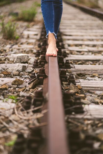 孤独一个穿着牛仔裤的女性赤脚穿过火车铁轨的垂直镜头轨道牛仔裤年轻