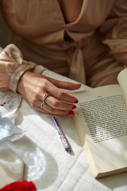 日光时尚的女人在家里拿着一本书抽红色指甲油优雅没有脸