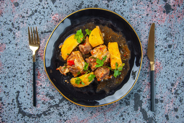 烤箱美味的晚餐俯视图 黑色盘子里放着绿色的肉土豆 餐具放在混合色的背景上餐具锅晚餐