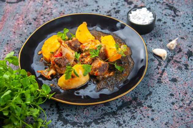 烤箱美味晚餐的侧视图 黑色盘子里放着绿色的肉土豆和混合色背景上的蒜盐盐肉食物