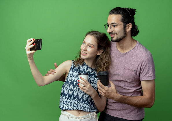 使用一对年轻的情侣热恋中 幸福的女人用智能手机在绿色背景上为他们拍照站立照片手机