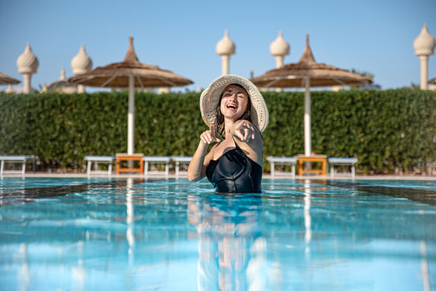 女孩一个穿着黑色泳衣戴着帽子的漂亮女孩在游泳池里洗澡在温暖的国家度假和娱乐的概念夏天享受度假村