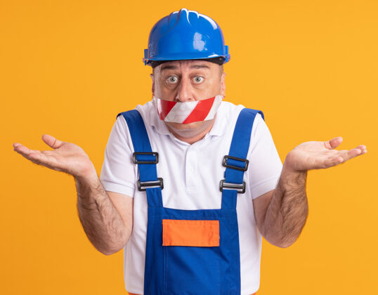 封面困惑的成年建筑工人穿着制服 用胶带捂住嘴巴 双手张开隔离在橙色的墙上感情姿势持有