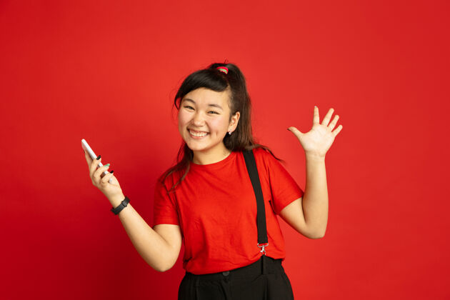 工作在红色工作室背景上孤立的亚洲青少年的肖像休闲风格的美丽的深褐色女性模特人类情感的概念 面部表情 销售 广告快乐 手持智能手机衬衫手势面部
