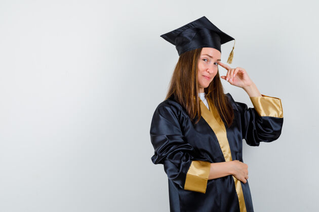 帽子女毕业生穿着学院服 手指放在太阳穴上 看起来很懂事 前视学术长袍成功