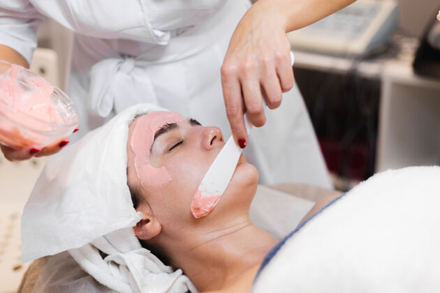 沙龙美容师用抹刀在女人脸上敷海藻酸钠面膜女性医学专业