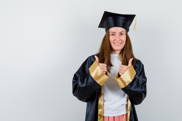 成就女毕业生穿着学院服竖起大拇指 看上去很快乐正面图双人女孩人
