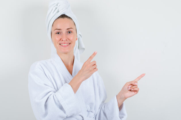 魅力年轻女士指着右上角 穿着白色浴衣 毛巾 看上去很愉快正视图浴袍成人健康