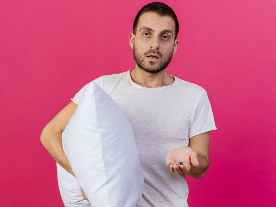 生病年轻的病夫抱着枕头 粉色背景上隔离着药片吃药抱枕年轻