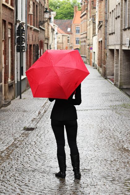 时尚街上一个拿着红伞的女人的垂直镜头美丽年轻背部