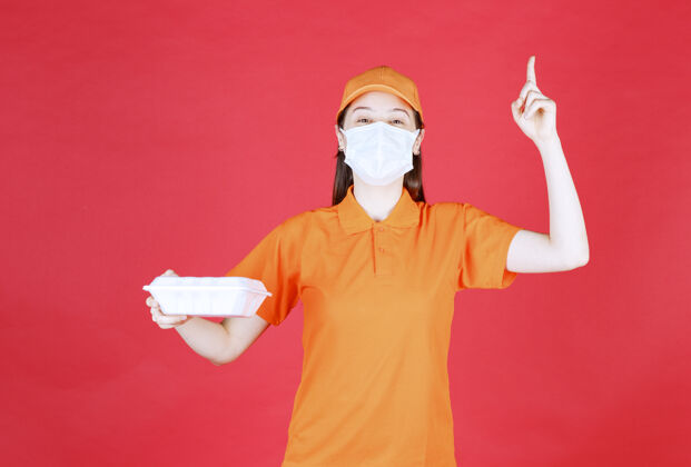 不确定身着橘色制服 戴着口罩的女服务人员手持外卖食品包 看上去若有所思 充满梦想女人厨师面具