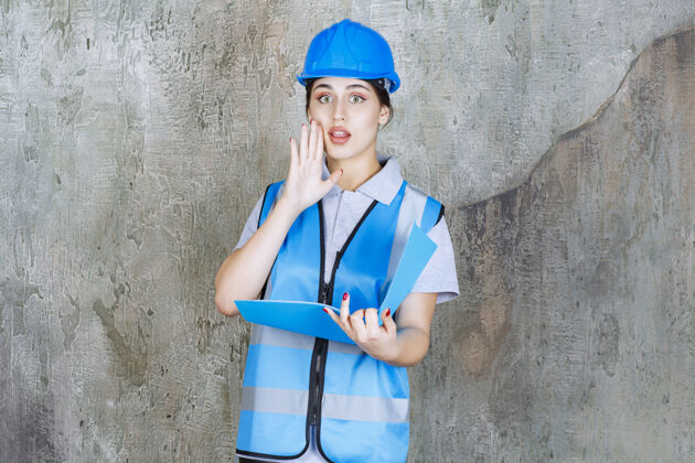 建筑身穿蓝色制服 头戴安全帽的女工程师拿着一个蓝色报告夹 说着一些私人的话制服清单员工