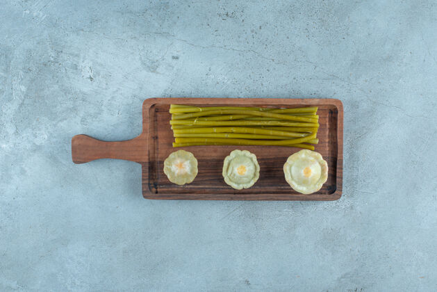 风味美味的腌制小南瓜和棍子放在大理石表面的木板上美味泡菜棒子