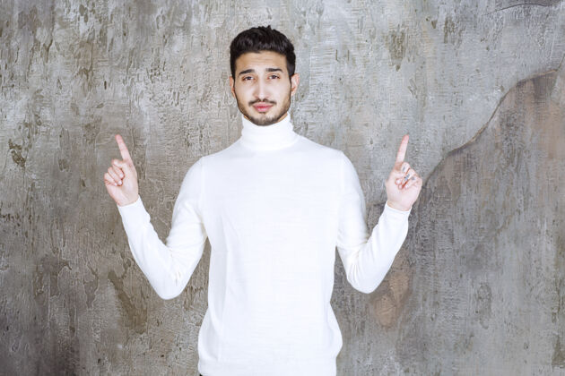 男人穿着白色毛衣的时装模特站在水泥墙上举手以示关注评论时髦允许