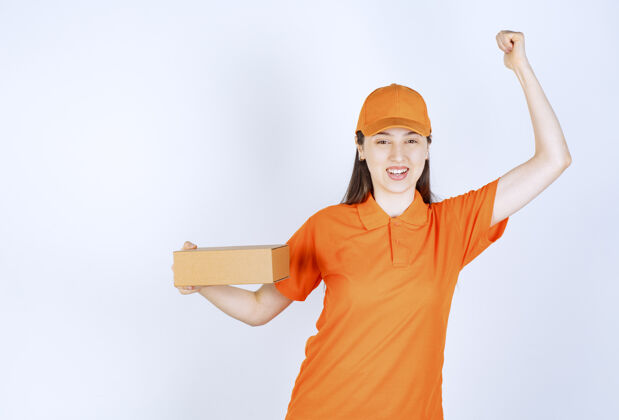 订单身着橙色制服的女服务人员手持一个纸板箱 并展示成功的手势制服邮件姿势
