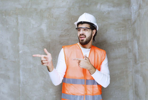 地点戴着白色头盔和护目镜的工程师指着他的同事或旁边的东西方向男性人