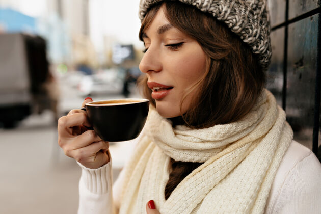 商业女性不规则剪裁的特写外景 迷人可爱的女孩 戴着针织帽子和围巾 喝着咖啡 享受着咖啡休息学生集中职业