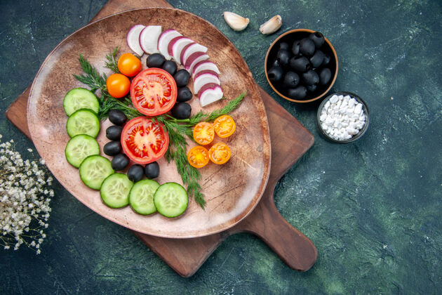 混合上图：棕色盘子里的新鲜切碎蔬菜放在木制砧板上橄榄放在碗里盐大蒜素花放在五颜六色的桌子上健康橄榄板