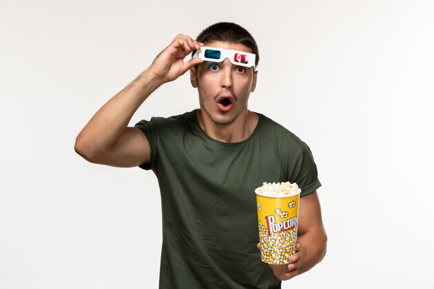 成人正面图身穿绿色t恤的年轻男性手持爆米花 戴着d墨镜在白墙电影《孤独电影院》上起飞男性电影电影采取电影