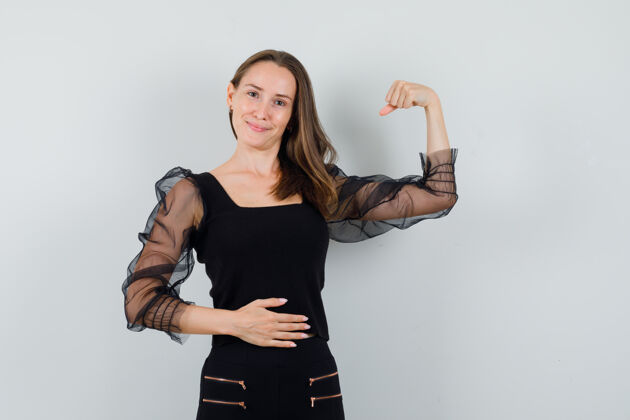 化妆一个穿着黑色上衣和黑色裤子的年轻女人 展示着她的肌肉 一只手放在肚子上 看起来很乐观健康干净护理