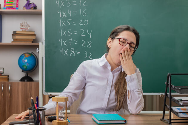 教室戴着沙漏和笔记本眼镜的年轻女老师学校累前面