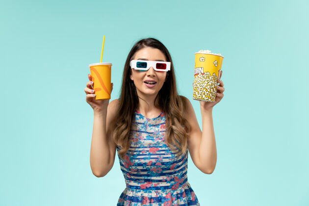 年轻女性正面图年轻女性 带着爆米花包 戴着d墨镜在蓝色表面喝酒电影剧院爆米花