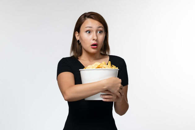 篮子正面图：年轻的女性拿着土豆片篮子 在浅白的表面上摆姿势举行电影院孤独