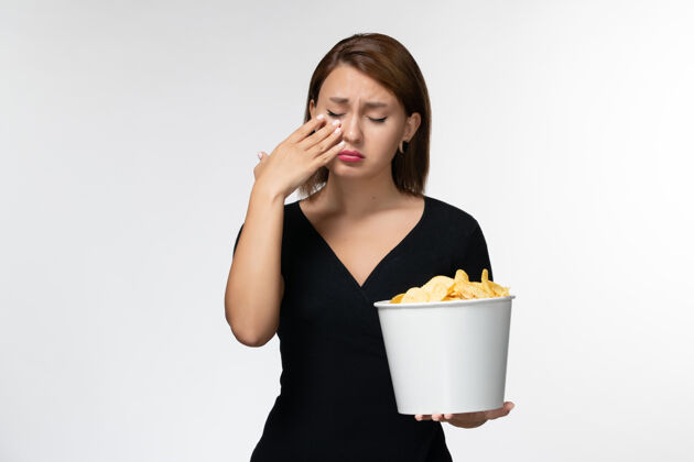 看正面图：年轻的女性拿着土豆片的篮子在白色的表面上看电影哭泣篮子哭剧院