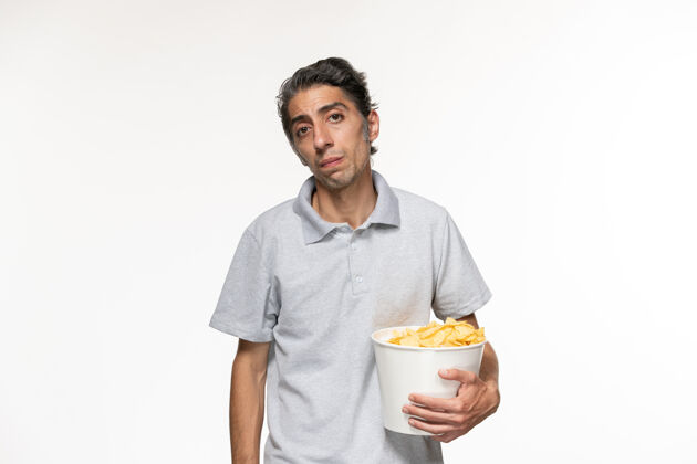 前面正面图：年轻男性一边吃薯片一边在白色表面上看电影看服务员电影院