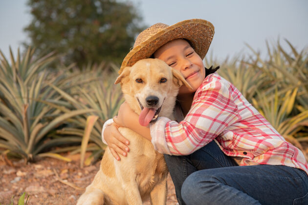 放松亚洲小女孩和狗快乐可爱的女孩 穿着牛仔裤 戴着帽子 在菠萝农场和狗玩耍 在乡村的夏天 童年和梦想 户外生活方式自然生活方式脸
