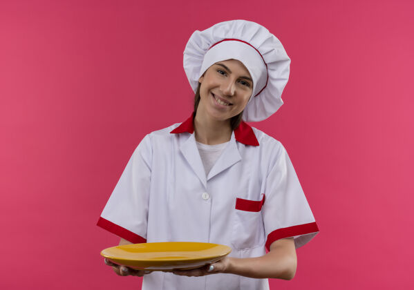 空间身着厨师制服 面带微笑的白人年轻厨师女孩拿着盘子隔离在粉色空间和复印空间复制盘子厨师