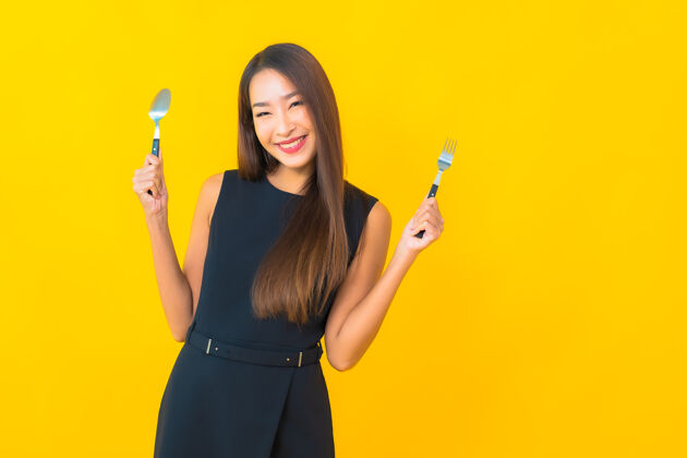 营养肖像美丽的亚洲年轻女子准备用叉子和勺子吃黄色背景肖像晚餐早餐