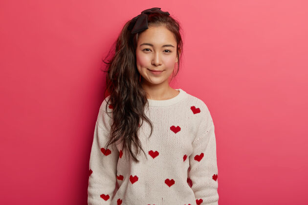 女性美丽温柔的亚洲女孩 长马尾 胭脂色脸颊 穿着舒适的心形套头衫 站在粉色背景下美丽皮肤黑发