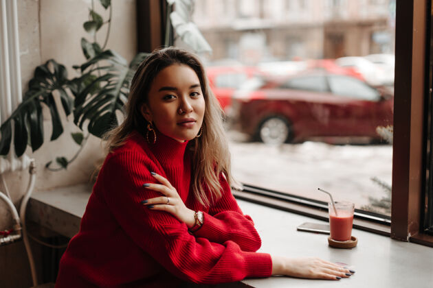 模特一位身穿红色针织毛衣 修着黑指甲的女士在咖啡馆靠窗的桌子前摆姿势魅力茶金发