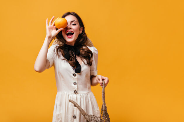 肖像白裙女士笑了 用橙色遮住眼睛 拿着橙色背景的环保袋水果手提包瘦身