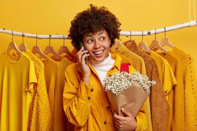 衣服快乐的卷发女人转身离开 通过手机打电话 分享购物日后的印象 摆出一束鲜花短信电子电话