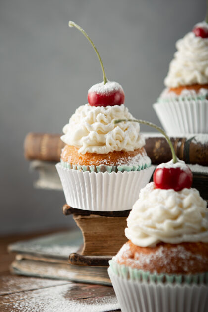 樱桃垂直拍摄美味的纸杯蛋糕与奶油 糖粉 樱桃上的书颜色背景传统