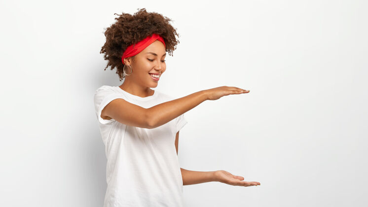 欢呼卷发女人展示某物的高度 用双手做手势 展示包裹的大小休闲穿着微笑