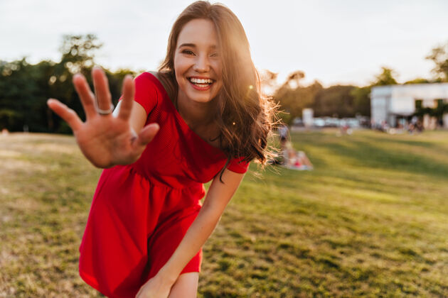 快乐阳光明媚的日子里 一位温文尔雅的白种女人对着镜头微笑一张身着红色连衣裙的快乐美丽女孩站在公园里的户外照片草年轻魅力