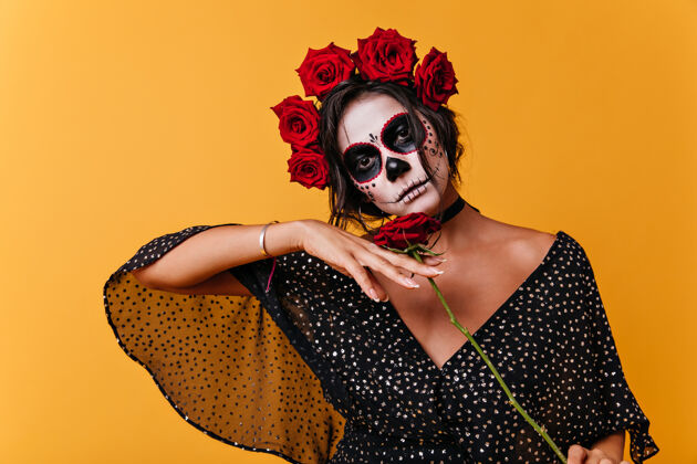 花悲伤的西班牙女孩在嘉年华的形象照片与玫瑰花冠在她的手拿着红花的女士在室内黑发化妆恐怖
