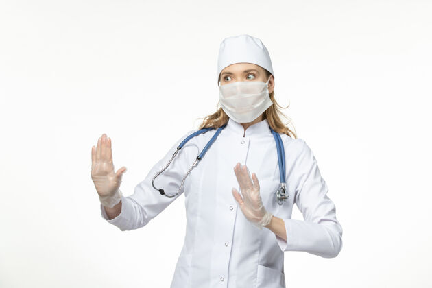医疗器械正面图女医生穿着医疗服戴着口罩和手套因冠状病毒白墙大流行病毒病套装大流行面罩