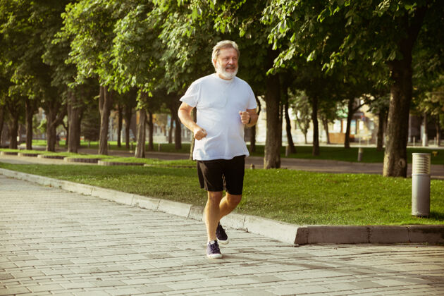 跑步高级男子作为跑步者与袖标或健身追踪器在城市的街道退休老年人耳机