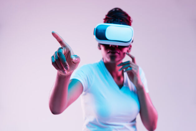 虚拟现实年轻的非洲裔美国妇女的肖像玩在虚拟现实眼镜在霓虹灯梯度背景小玩意游戏面部